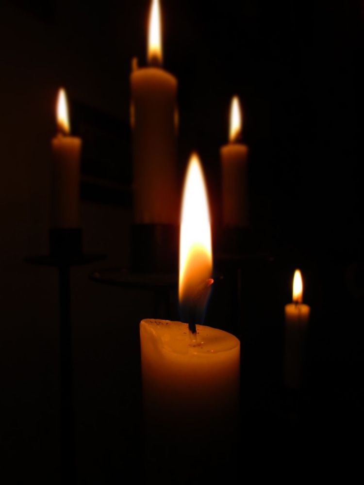 Mehrere brennende Kerzen leuchten warm in einem dunklen Raum.